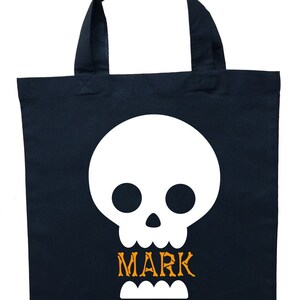 Puede incluir: Una bolsa de lona negra con una calavera blanca y el nombre "MARK" en letras naranjas.