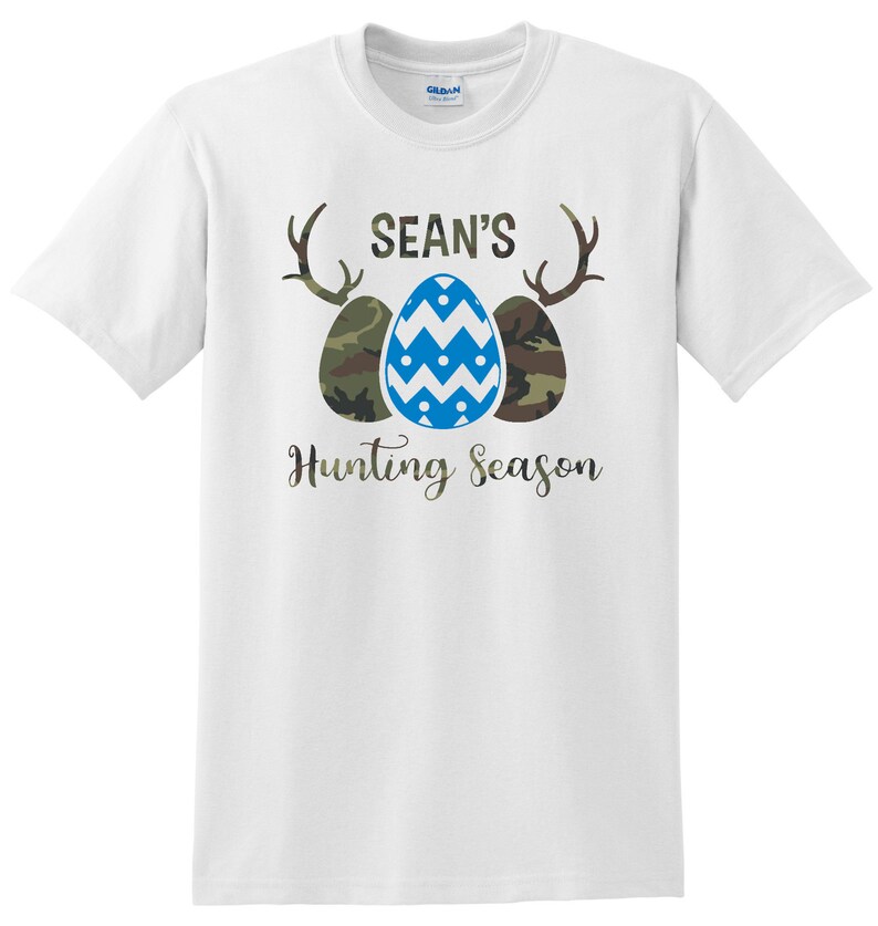 May include: White t-shirt with a blue and green camouflage pattern Easter egg design. The text "SEAN'S Hunting Season" is printed below the eggs.