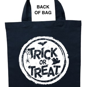 K&ouml;nnte beinhalten: Eine schwarze Stofftasche mit einem wei&szlig;en Kreisdesign, auf dem "Trick or Treat" mit einer Spinne, einer Fledermaus und einem Blatt steht. Die Tasche hat schwarze Henkel.
