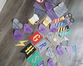 May include: A collection of assorted paper cutouts for photo props, including heart-shaped signs with text, pennants labeled Team Bride and Team Groom, a lightning bolt, a ring, glasses, ties, and beer mugs, featuring various phrases and colors.
