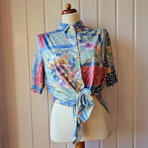May include: A blue, red, and green floral patterned shirt with a button-up front and short sleeves. The shirt is tied at the waist.