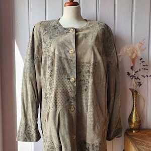 Könnte beinhalten: Eine braune Wildlederjacke mit floralem Muster und Knopfleiste. Die Jacke hat eine lockere Passform und ist aus einem weichen, bequemen Material gefertigt.