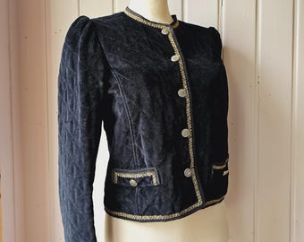 May include: A vintage black velvet jacket with quilted sleeves and a tailored fit. The jacket features gold trim along the collar, pockets, and button closures. The jacket is displayed on a mannequin.