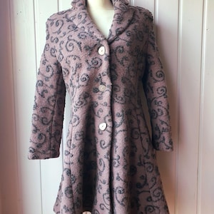May include: Mauve coat with a dark grey swirling pattern. The coat features a wide collar, three large white buttons, and a flared skirt. The garment is displayed on a mannequin. The background is white.