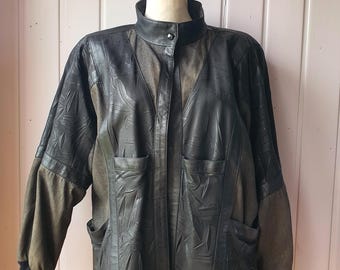 May include: A dark charcoal gray leather jacket featuring a high collar with a single snap button closure, long sleeves with ribbed cuffs, and two front pockets. The jacket displays a textured leaf-like pattern on the leather panels.
