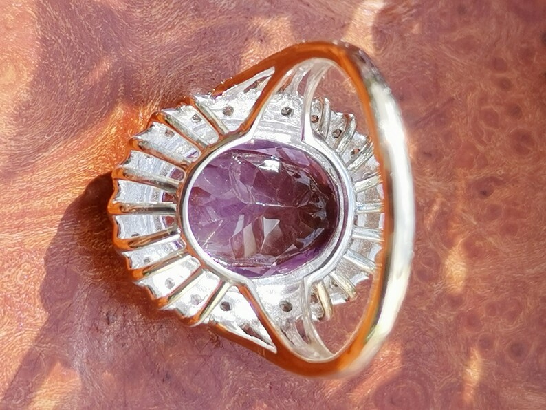 Op de afbeelding: Een zilveren ring met een grote ovale amethist-edelsteen omringd door kleinere diamanten. De ring heeft een delicate band.