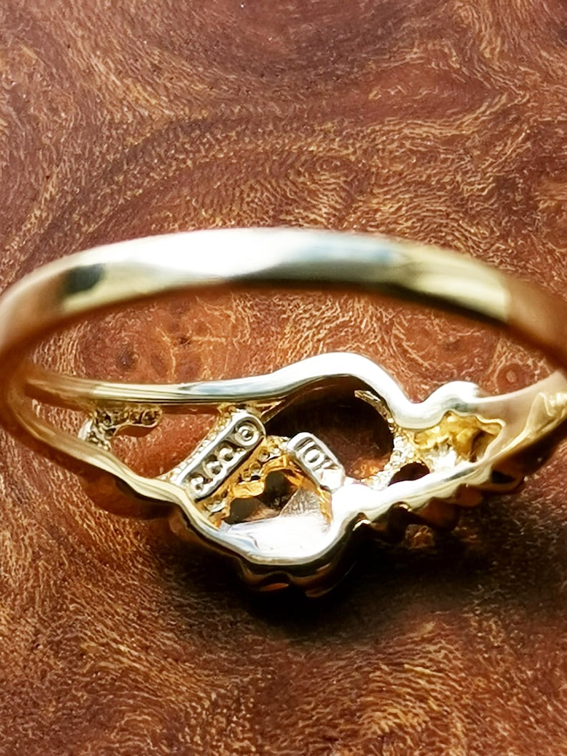 May include: A gold ring with a detailed design. The ring is marked "10K" and "GGG" on the inside.