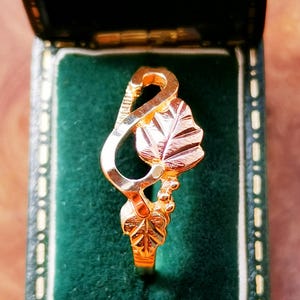 May include: A gold ring with a leaf design. The ring is in a green velvet box.