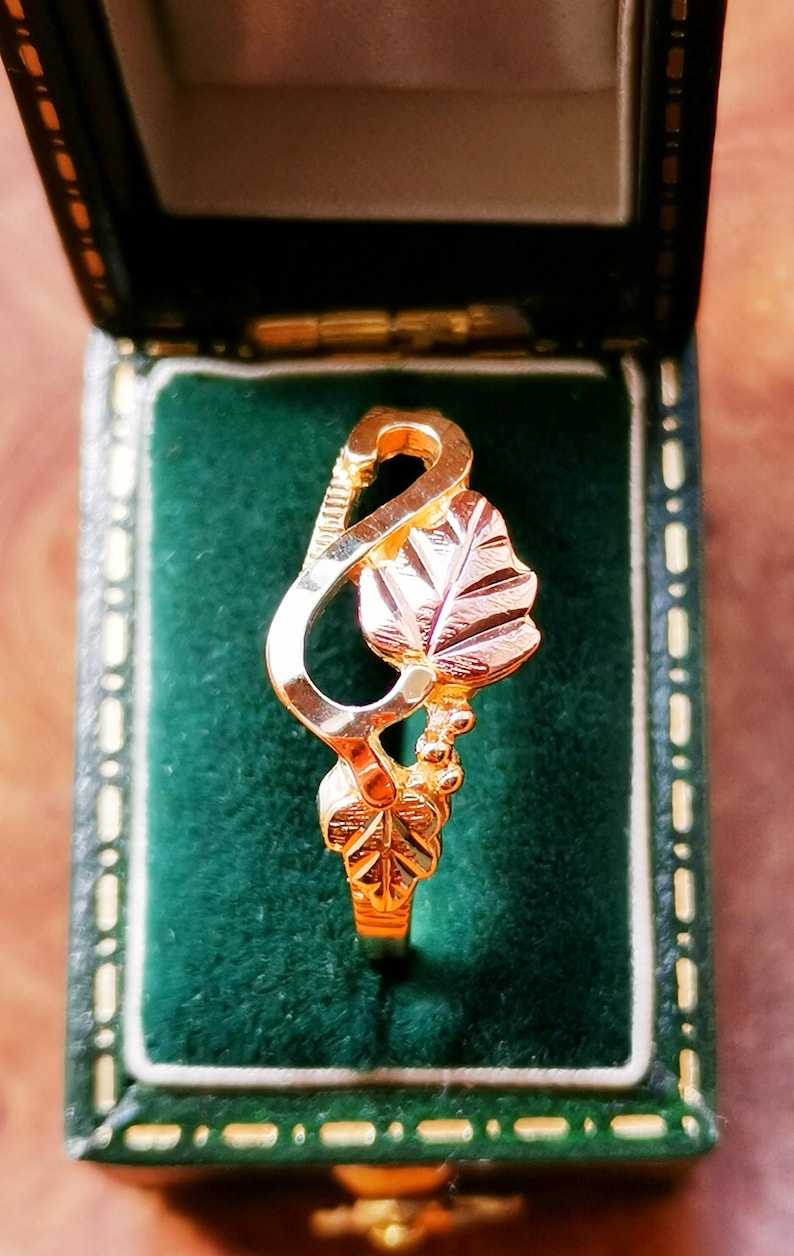 May include: A gold ring with a leaf design. The ring is in a green velvet box.