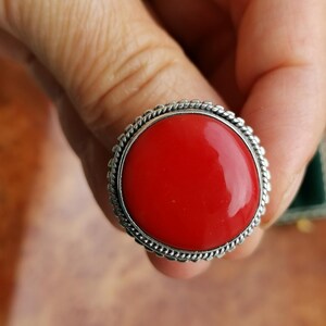 Pode incluir: Um anel de prata com uma grande gema redonda vermelha engastada em uma moldura de prata decorativa.