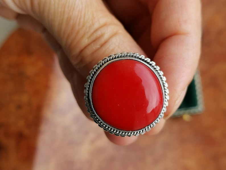 Pode incluir: Um anel de prata com uma grande gema redonda vermelha engastada em uma moldura de prata decorativa.