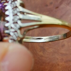 Op de afbeelding: Close-up van de binnenkant van een gouden ring met een paarse edelsteen en kleine diamanten. De ring is gemarkeerd met "9ct 375".