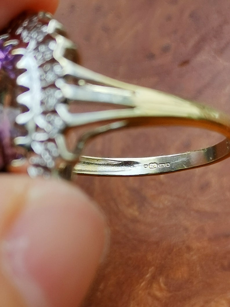 Op de afbeelding: Close-up van de binnenkant van een gouden ring met een paarse edelsteen en kleine diamanten. De ring is gemarkeerd met "9ct 375".
