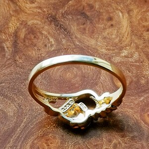 May include: A gold ring with a floral design and a clear stone in the center. The ring is on a wooden surface.