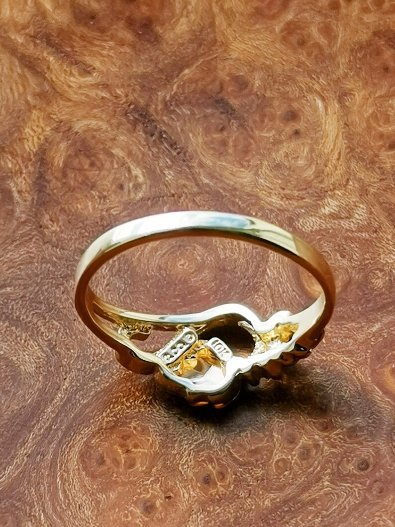 May include: A gold ring with a floral design and a clear stone in the center. The ring is on a wooden surface.