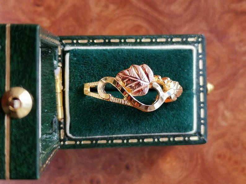 May include: A gold ring with a red and green leaf design. The ring is in a green velvet ring box.