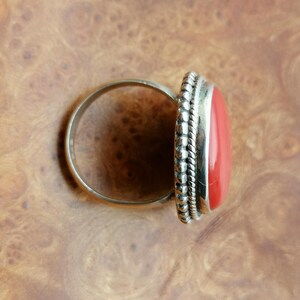 Pode incluir: Um anel de prata com uma grande pedra vermelha ovalada engastada em uma moldura de contas.