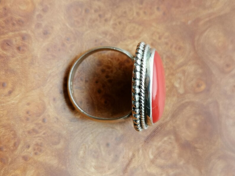 Pode incluir: Um anel de prata com uma grande pedra vermelha ovalada engastada em uma moldura de contas.