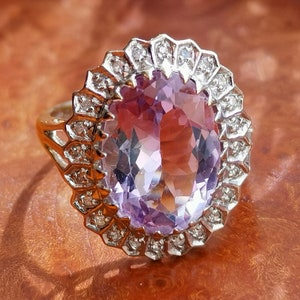 Op de afbeelding: Een ring met een grote ovale amethist-edelsteen, omringd door een halo van kleinere diamanten.