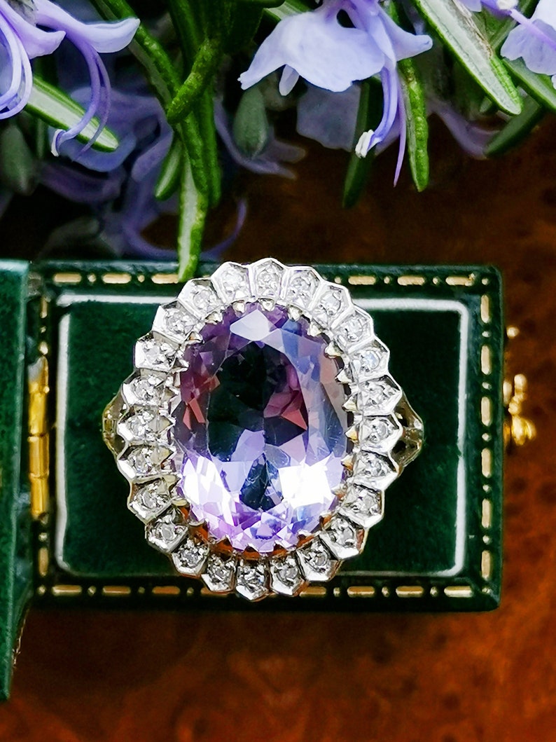 Op de afbeelding: Een ring met een paarse amethist en een halo van diamanten. De ring ligt in een groene fluwelen ringdoos.