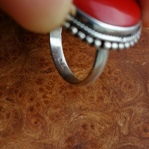 Pode incluir: Close-up de um anel de prata com uma pedra oval vermelha. O anel &eacute; marcado com o n&uacute;mero "925" na banda interna.