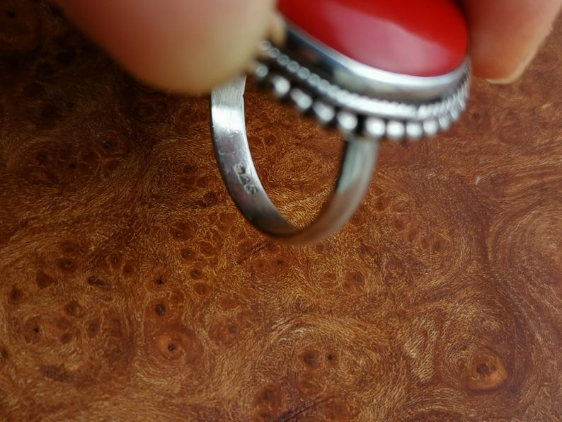 Pode incluir: Close-up de um anel de prata com uma pedra oval vermelha. O anel &eacute; marcado com o n&uacute;mero "925" na banda interna.