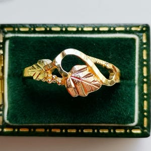 May include: A gold ring with a leaf design. The ring is set in a green velvet box.
