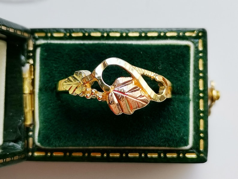 May include: A gold ring with a leaf design. The ring is set in a green velvet box.