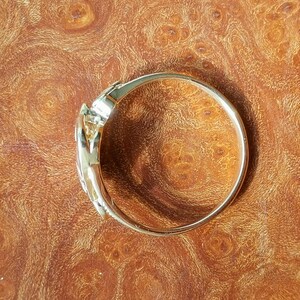 May include: A gold-toned bangle bracelet with a unique, twisted design. The bracelet is smooth and shiny, and it appears to be made of metal.