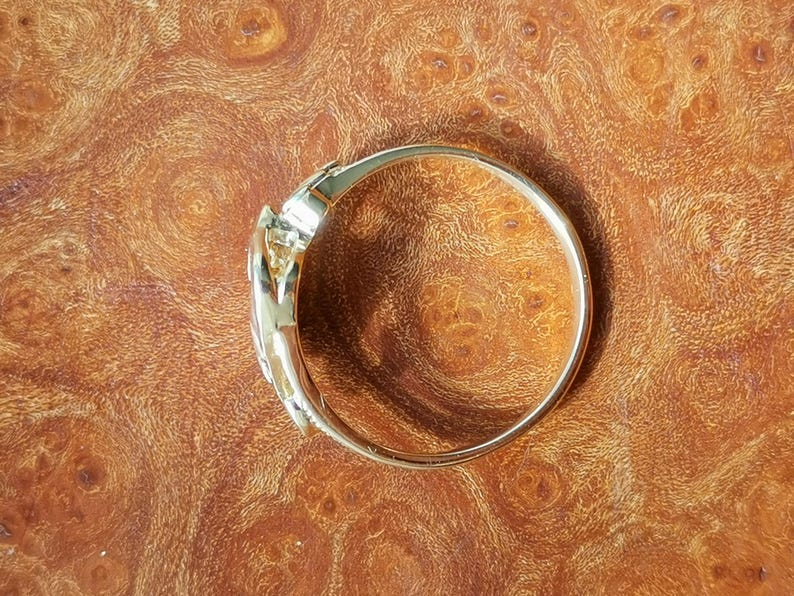 May include: A gold-toned bangle bracelet with a unique, twisted design. The bracelet is smooth and shiny, and it appears to be made of metal.