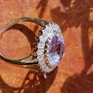 Op de afbeelding: Een gouden ring met een grote ovale amethist-edelsteen omringd door een halo van kleinere diamanten.