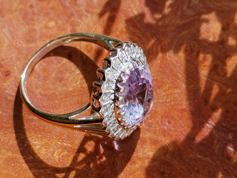 Op de afbeelding: Een gouden ring met een grote ovale amethist-edelsteen omringd door een halo van kleinere diamanten.