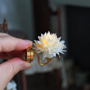 Peut inclure: Une applique murale miniature avec une fleur blanche et un centre chaleureux et lumineux. L'applique a une base et un bras en métal doré, conçus pour une maison de poupée ou un cadre miniature.