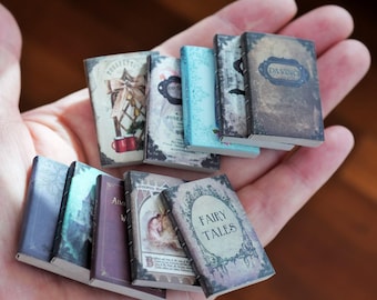 May include: A collection of miniature books with aged covers, held in a hand. The books feature titles like "Fairy Tales" and "Da Vinci," with detailed illustrations and decorative elements. The books are various colors, including blue, purple, and brown.