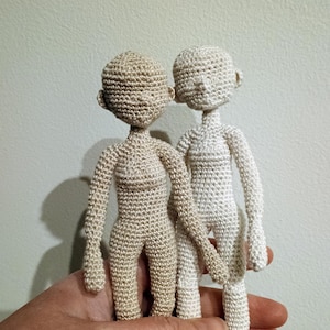 Könnte beinhalten: Zwei gehäkelte Puppen, eine in beige und die andere in weiß, stehen nebeneinander. Die Puppen halten sich an den Händen und haben keine Gesichtszüge.