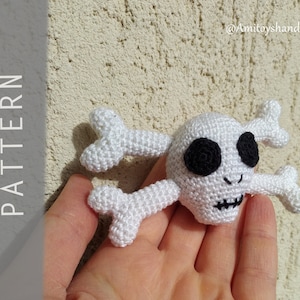 Puede incluir: Calavera y huesos cruzados de crochet blanco con ojos negros. La calavera tiene una boca cosida y una pequeña sonrisa. Los huesos cruzados tienen forma de corazón.