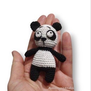 Puede incluir: Un pequeño juguete de panda de crochet con pelaje blanco y negro. El panda tiene ojos grandes y redondos y una nariz negra.