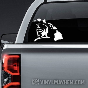 May include: White vinyl decal of a warrior's head with a helmet and the outline of the state of Hawaii. The decal is on the back window of a silver pickup truck.