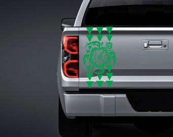 May include: A bright green vinyl decal applied to the tailgate of a silver pickup truck. The design features a central sea turtle motif integrated with a hibiscus flower, flanked by vertical rows of solid green triangles pointing downward.