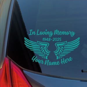 May include: A teal blue car window decal with the text "In Loving Memory 1948-2025" and two angel wings. The text "Your Name Here" is below the wings.