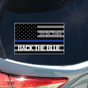 May include: A black and white American flag with a thin blue line across the middle. The flag has the words "We the People" written on it. The words "Back the Blue" are written below the flag.