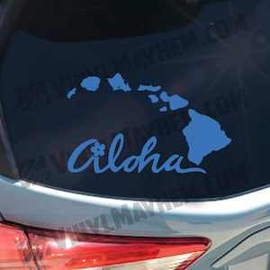 May include: A blue vinyl decal of the Hawaiian islands with the word "Aloha" in a cursive font with a small flower design. The decal is on the back window of a car.