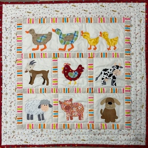 May include: A square quilted wall hanging featuring a grid of nine panels with fabric appliqués of farm animals including ducks, a goat, a chicken, a cow, a sheep, a pig, and a dog. The quilt has a white background with colourful striped borders.