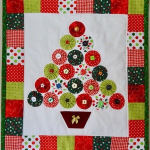 May include: A handmade Christmas tree wall hanging made with fabric scraps and buttons. The tree is green, red, and white with a brown felt base.