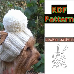 May include: A white knitted dog hat with two pom-poms on top. The hat is on a small brown dog's head. The image also includes a line drawing of a ball of yarn with knitting needles.