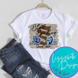 May include: White t-shirt with a brown and black graphic that says "Blood Brothers" with a stylized number 5 and the text "Damon Salvatore Stefan Salvatore Since 1864".