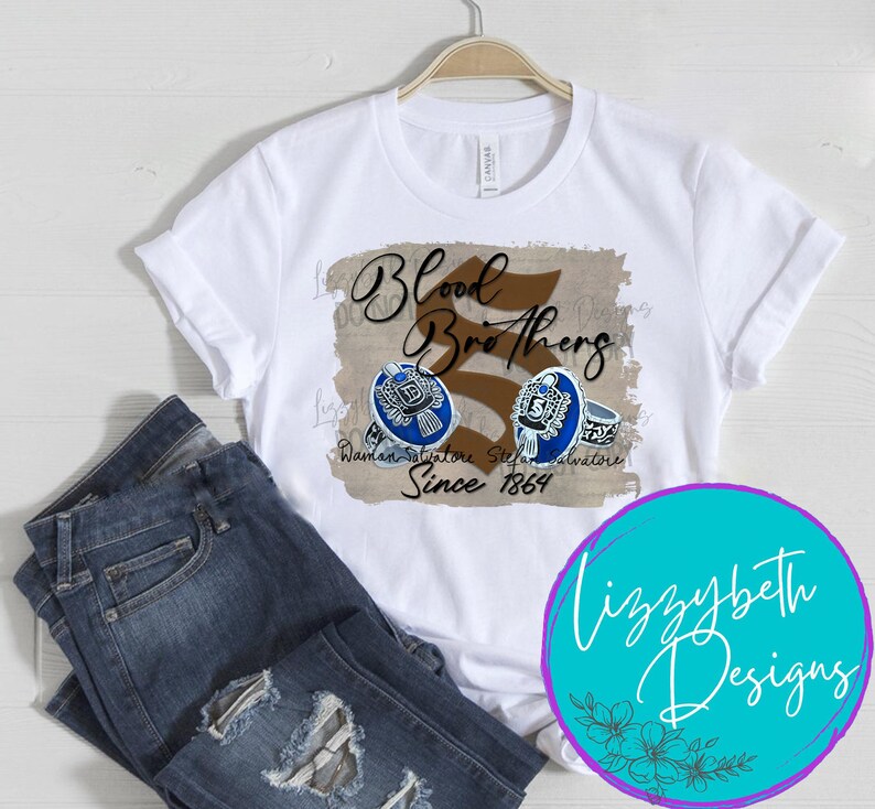 May include: White t-shirt with a brown and black graphic that says "Blood Brothers" with a stylized number 5 and the text "Damon Salvatore Stefan Salvatore Since 1864".