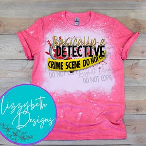 May include: Pink bleached t-shirt with a graphic design that says "Basically a Detective" with a yellow crime scene tape that says "Crime Scene Do Not Cross".