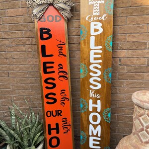 Op de afbeelding: Twee houten borden met de woorden "God Bless Our Home" en "God Bless This Home & All Who Enter" in witte letters. De borden zijn versierd met turquoise bloemen en een wit kruis bovenop het bord rechts.