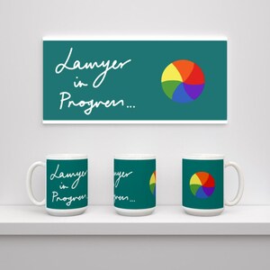 May include: Three white mugs with a teal green design. The mugs feature the text "Lamyer in Progress..." and a rainbow colored circle.